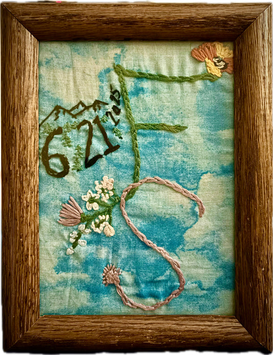 Custom Framed Embroidery Design - Perfect Wedding Gift, Wedding Keepsake, Birth Announcement, Special Dates, shown is an embroidered F+S with a date, flowers, mountains, and other small details included on a blue cloud background inside a wooden frame